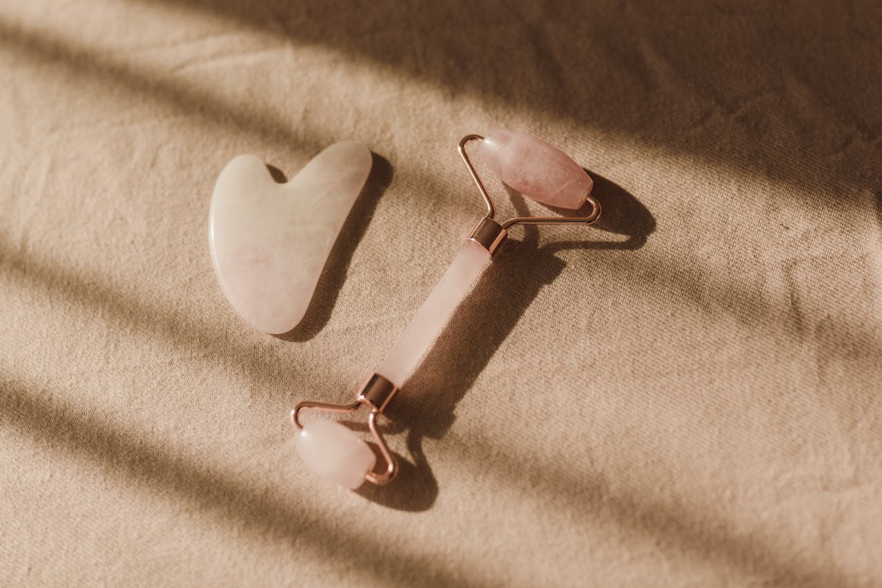 Elegant rose quartz facial roller and gua sha laid out on a beige fabric surface with soft lighting.